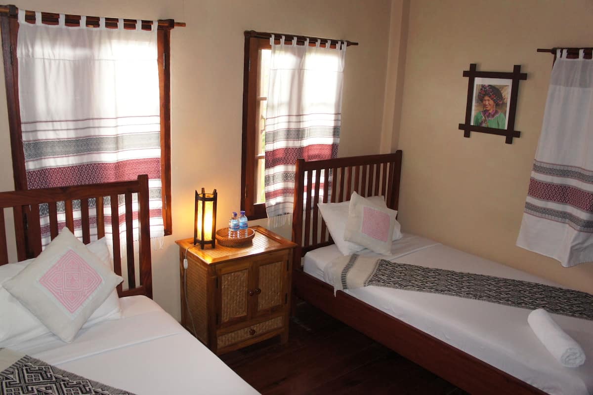 A room with two single beds, wooden headboards, a nightstand with a lamp, and a framed picture on the wall.