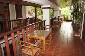 A covered outdoor area with wooden furniture, including tables and chairs, and a potted plant. - Lao Lu Lodge (Luang Prabang)