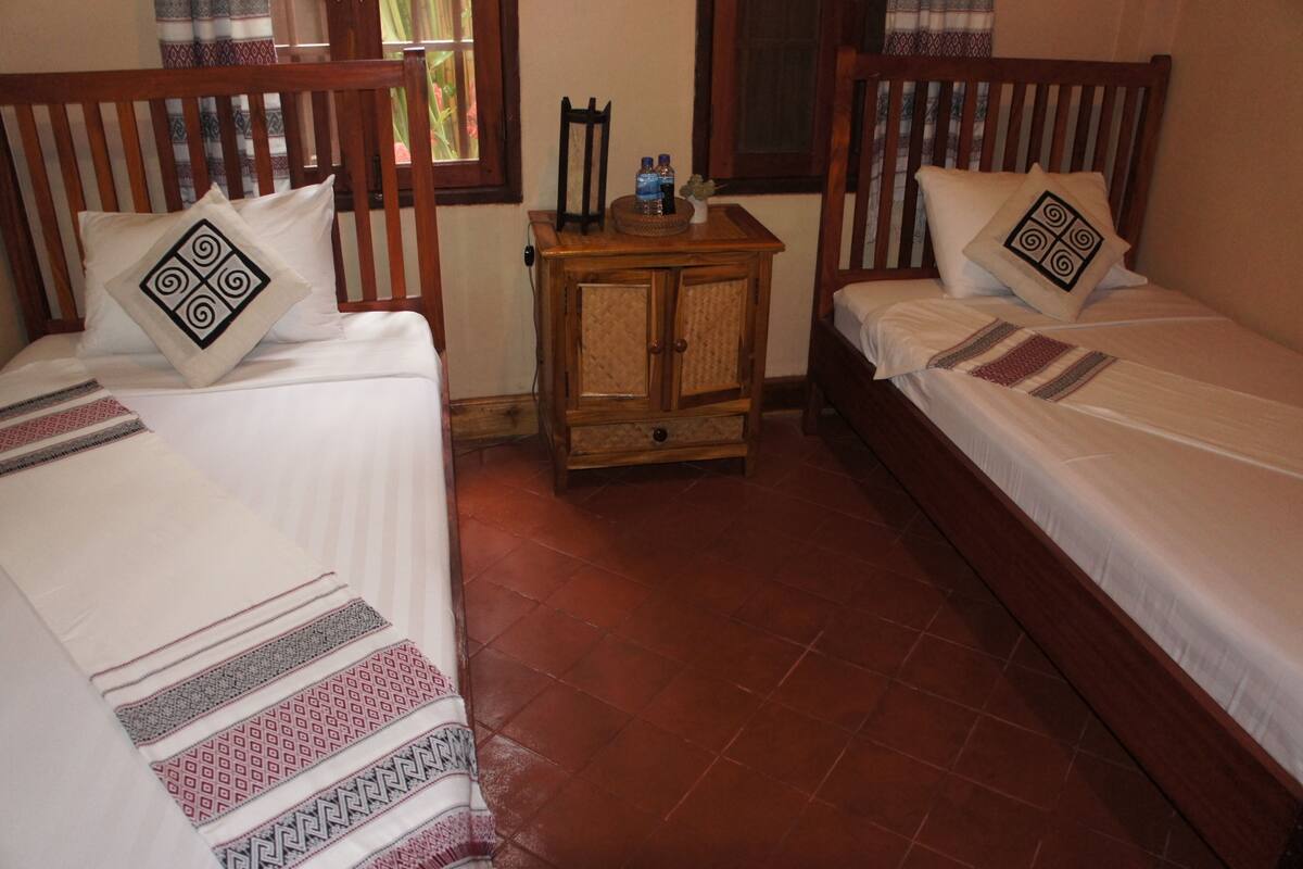 A room with two single beds, wooden headboards, a small wooden nightstand with a mirror, and a tiled floor.