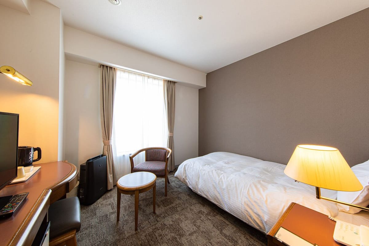 Ein Hotelzimmer mit einem Bett, einem Schreibtisch mit Computer und Kaffeemaschine, einem Sessel, einem kleinen Tisch und einer Lampe.
