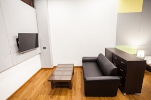 A modern living room with a flat-screen TV mounted on the wall, a glass-top coffee table, a black leather sofa, and a dark wooden dresser. - Admire Thonburi (Bangkok)