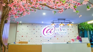 A reception desk with a logo, a wall with circular patterns, and a tree with pink flowers. - Admire Thonburi (Bangkok)