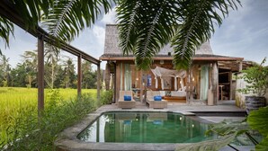 A poolside area with a lounge chair, a small table, and a potted plant. - Blue Karma Dijiwa Ubud (Ubud)