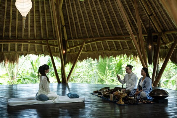 A traditional setting with a thatched roof, a mat on the floor, and a table with various items. - Blue Karma Ubud (Ubud)