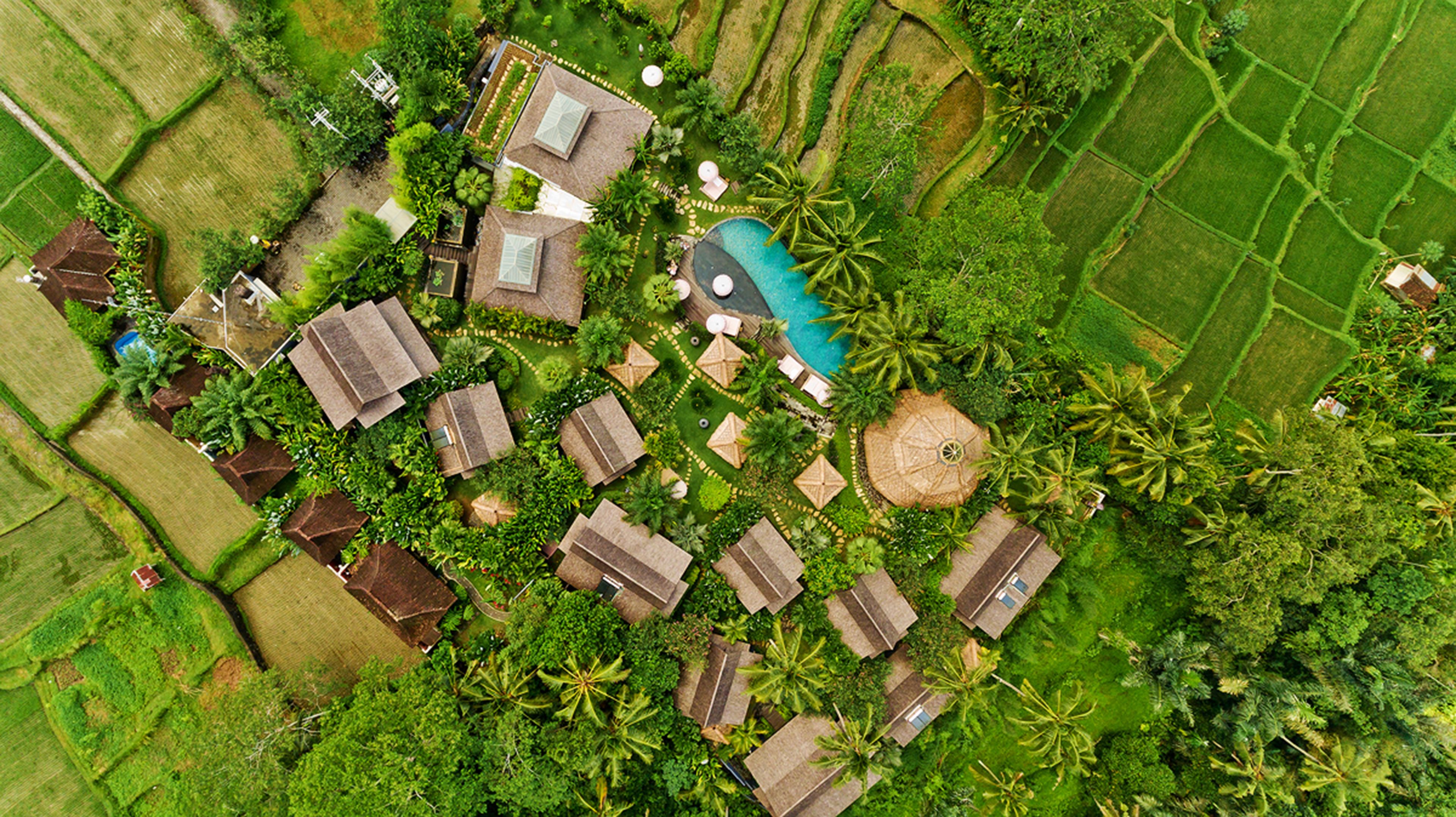 An aerial view of a resort with multiple bungalow-style accommodations, a swimming pool, and lush greenery.