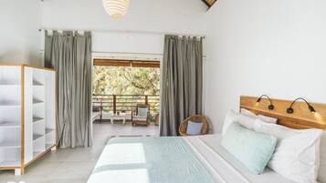 A bedroom with a bed, a wardrobe, a balcony with a view of trees, and a hanging light fixture.