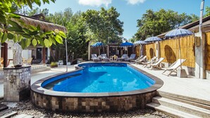 Una piscina con sillones de descanso y sombrillas, rodeada por una valla de madera y escalones de piedra.