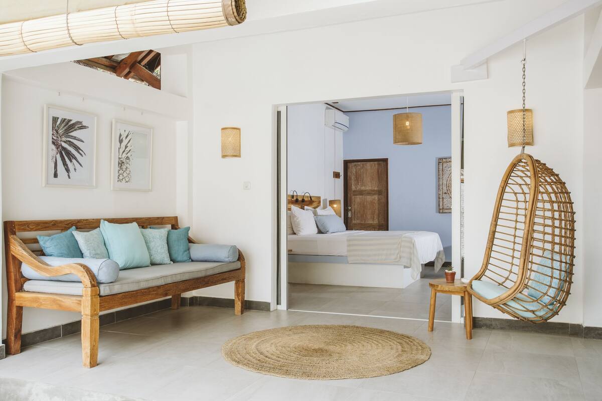 A room with a wooden bench, a hanging chair, and a bed with a white headboard.