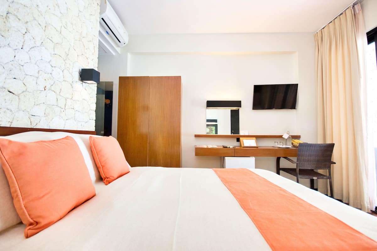 A hotel room with a bed, a desk, a mirror, and a TV.