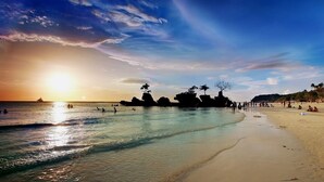 A beach with clear waters, a sunset, and rocky formations. - Watercolors Boracay Dive Resort (Boracay Island)