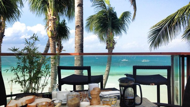 A dining table set with bread, coffee, and tea, overlooking a beach with palm trees and the sea. - Watercolors Boracay Dive Resort (Boracay Island)