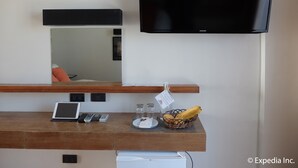 A hotel room with a wooden desk, a flat-screen TV, a laptop, a smartphone, a basket of bananas, a glass of water, and a small sign. - Watercolors Boracay Dive Resort (Boracay Island)