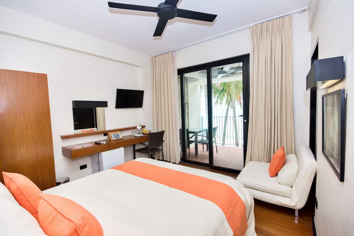 A hotel room with a bed, a desk, a chair, a TV, and a balcony with curtains.