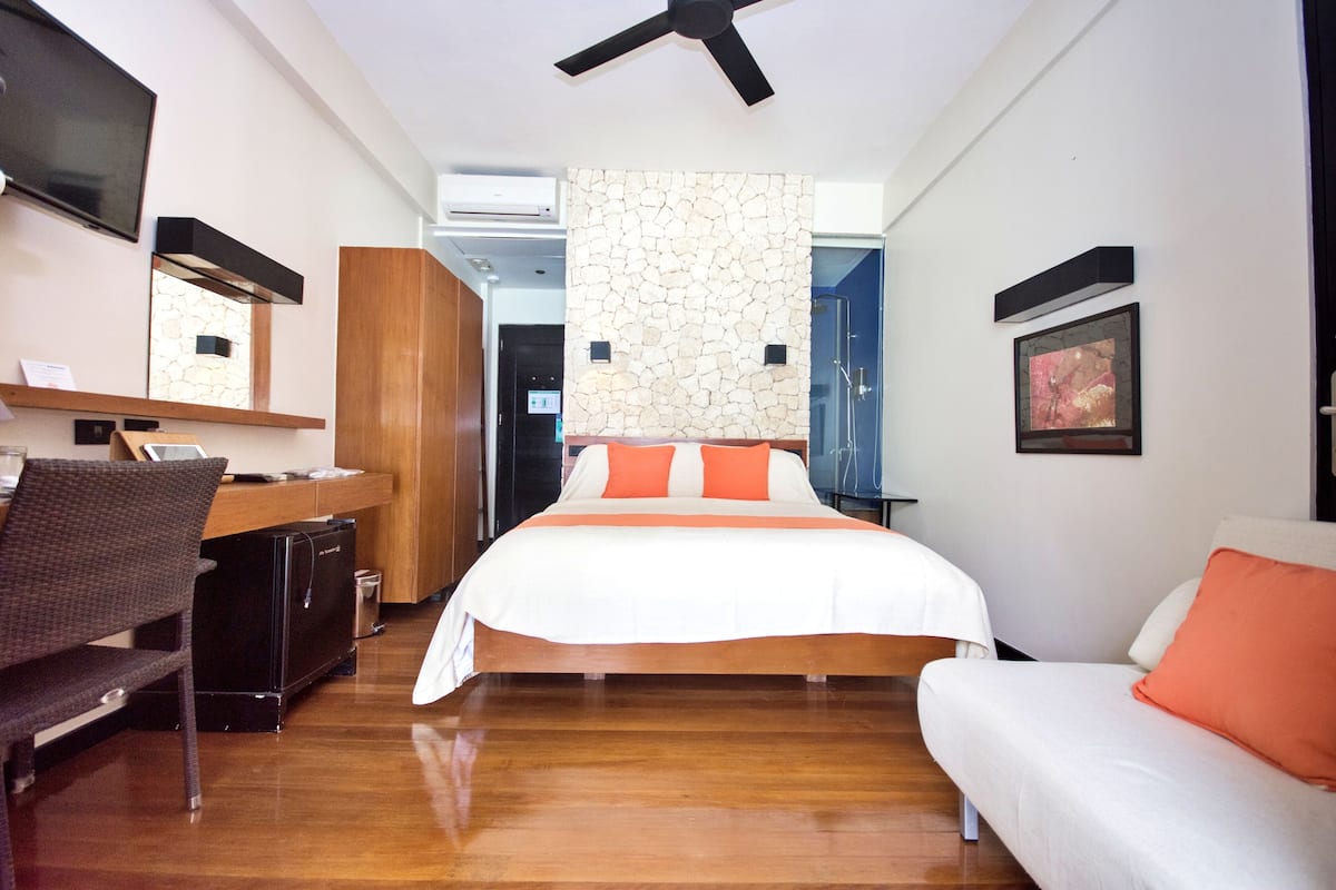 A modern hotel room with a bed, a desk, a chair, a TV, and a ceiling fan.