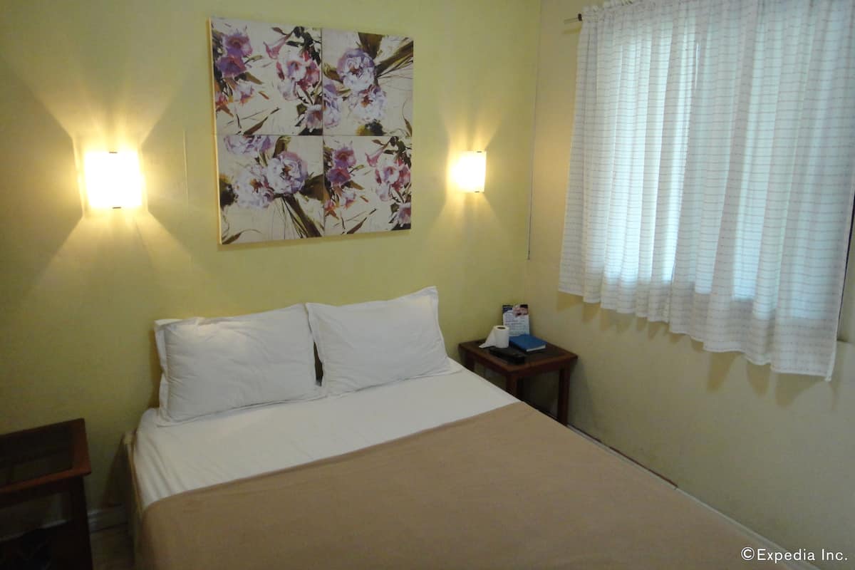 Une chambre d’hôtel avec un lit, une table de chevet, un tableau accroché au mur et une fenêtre avec des rideaux.