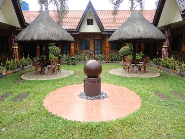 A courtyard with two thatched-roof structures, a central decorative sphere, and surrounding seating areas.
