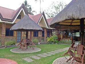 A bungalow with a thatched roof, a stone facade, and a garden with a paved walkway.