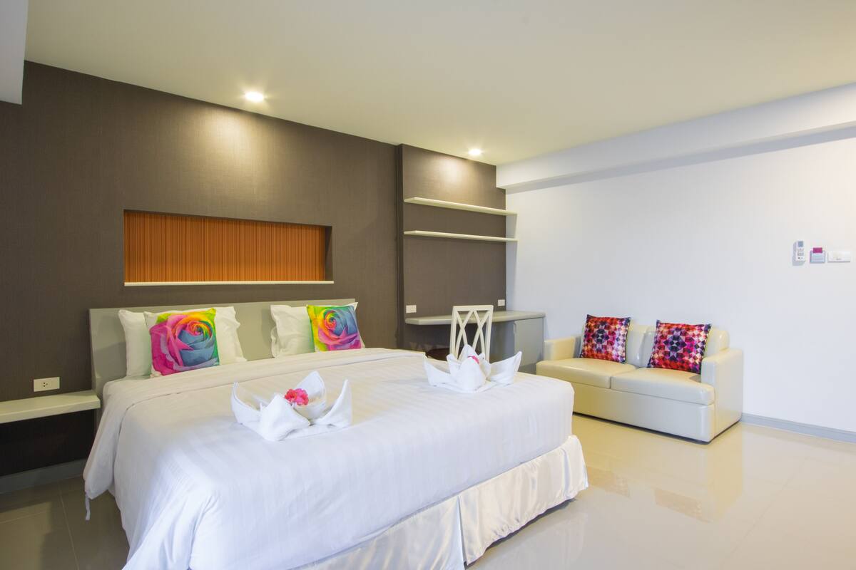 Een moderne hotelkamer met een groot bed, een witte bank en een ingebouwde wandplank.