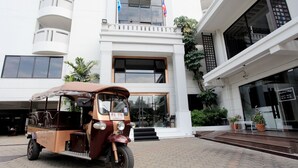 Un tuk-tuk estacionado frente a un edificio moderno con ventanas amplias y un balcón.