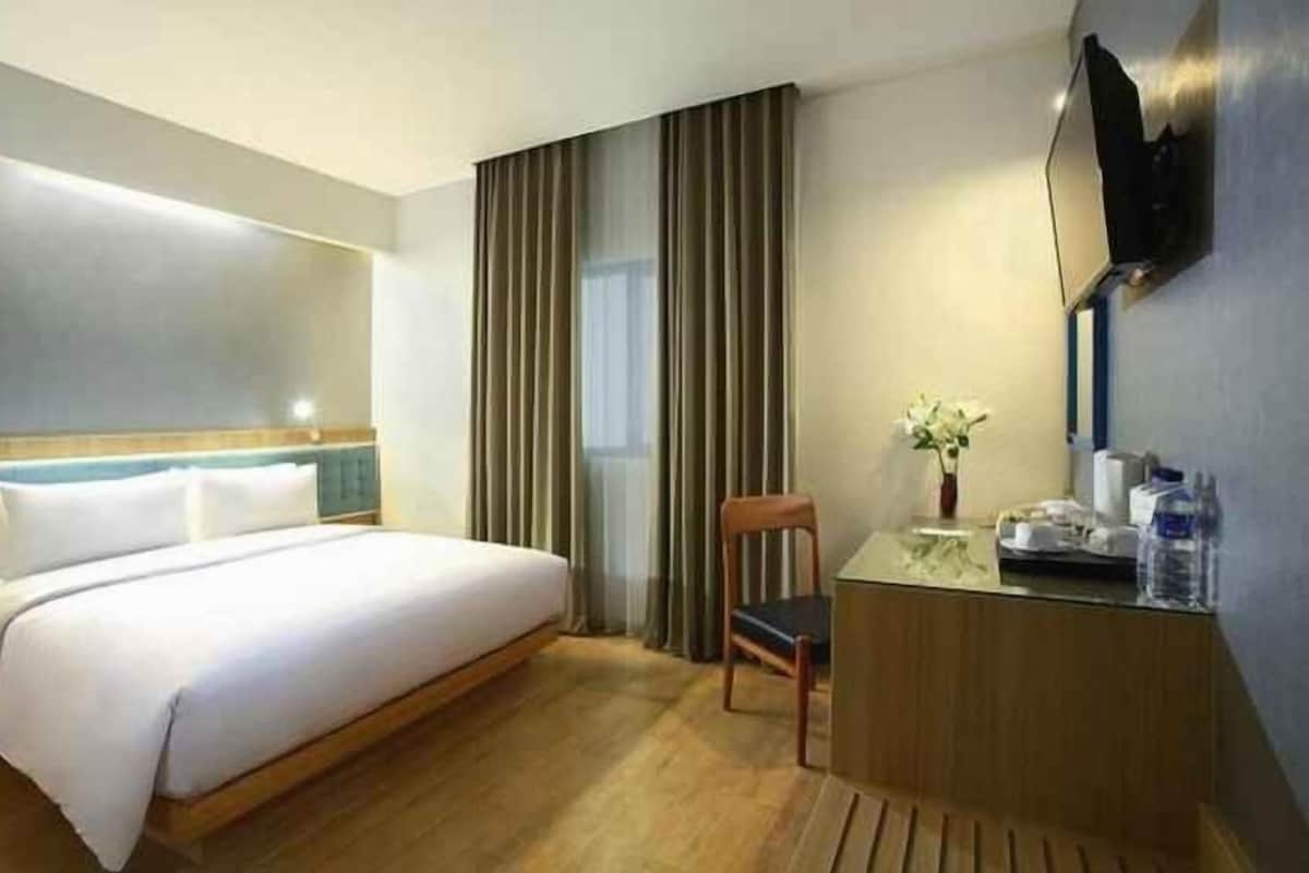 Une chambre d’hôtel avec un lit, un bureau, une chaise, une télévision et une fenêtre avec des rideaux.