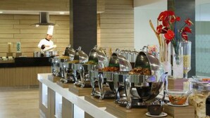 Un buffet avec plusieurs présentoirs de nourriture, un chef en uniforme et des fleurs décoratives.