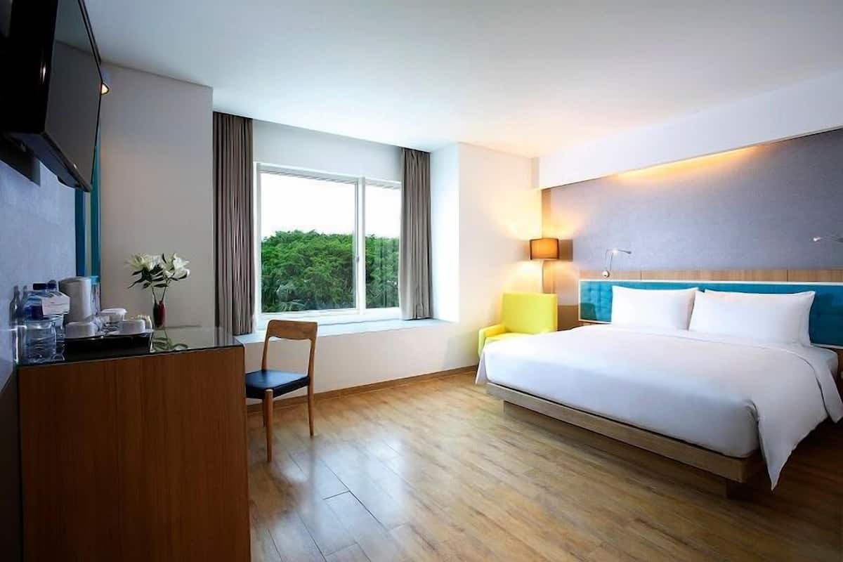 Une chambre d’hôtel équipée d’un lit, d’un bureau, d’une chaise, d’une lampe et d’une fenêtre donnant sur un paysage verdoyant.
