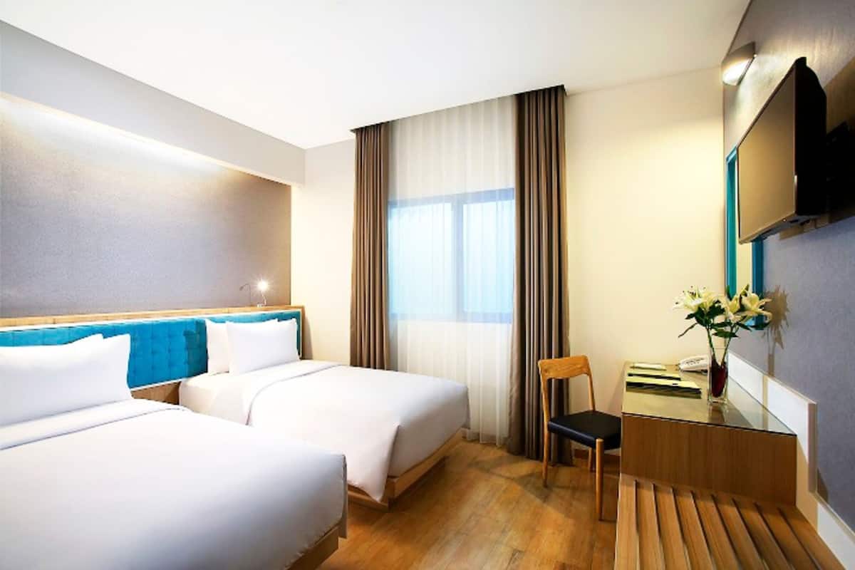 Une chambre d’hôtel avec deux lits, un bureau, une chaise, une télévision et une fenêtre avec des rideaux.