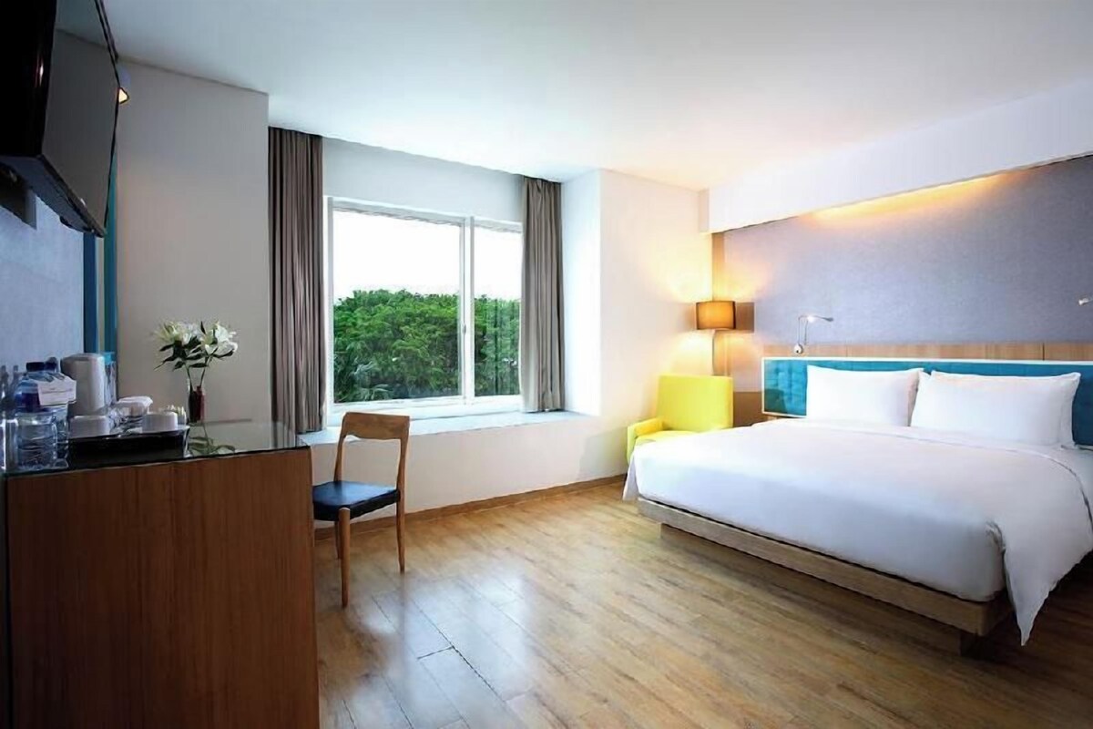 Une chambre d’hôtel avec un lit, un bureau, une chaise, une fenêtre avec des rideaux et une lampe.
