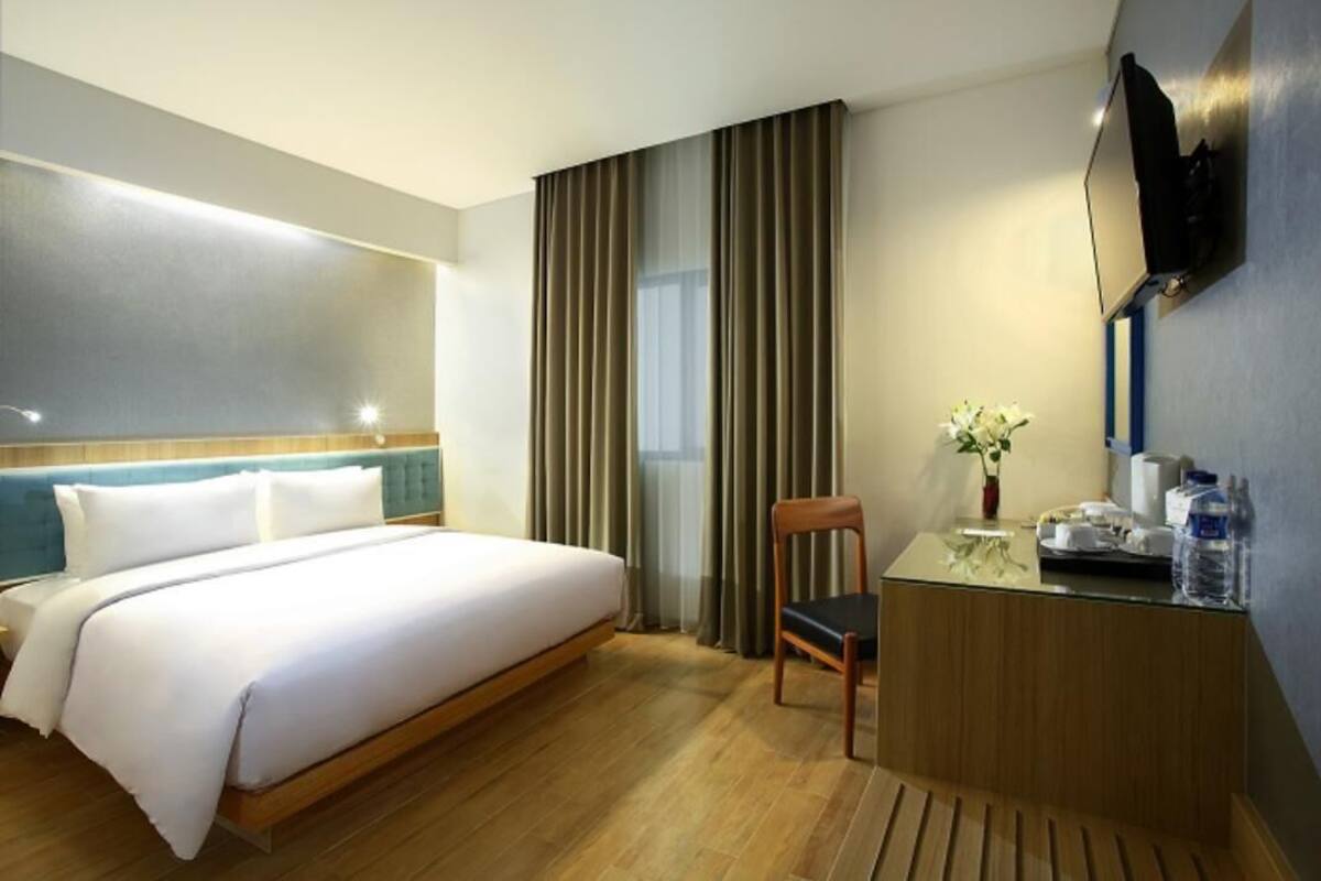 Une chambre d’hôtel comprenant un lit, un bureau avec une chaise, une télévision et une fenêtre avec des rideaux.