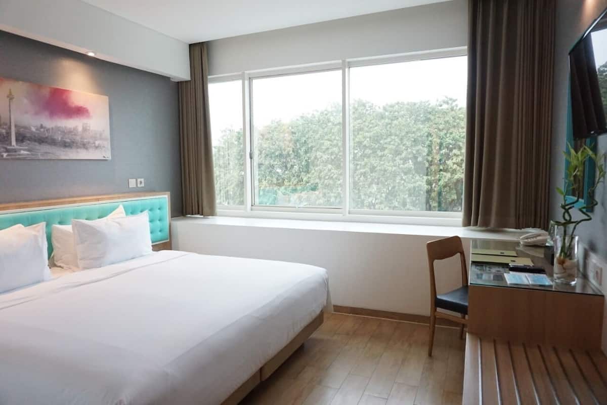 Une chambre d’hôtel avec un lit, un bureau, une chaise, une fenêtre avec des rideaux et un tableau au mur.