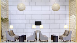 Un hall d’entrée au design moderne, comprenant un espace salon avec deux fauteuils et un canapé, un téléviseur à écran plat fixé au mur, ainsi que deux tables rondes avec des lampes.