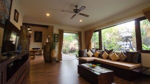 A spacious living area with a wooden floor, a sofa with cushions, a coffee table, and a ceiling fan. - Villa Nesanur (Denpasar)