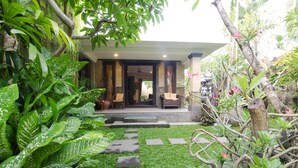 A tropical garden leading to a building with a covered entrance and seating area. - Villa Nesanur (Denpasar)
