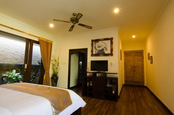 A bedroom with a bed, a television, a ceiling fan, and a door leading to another room.