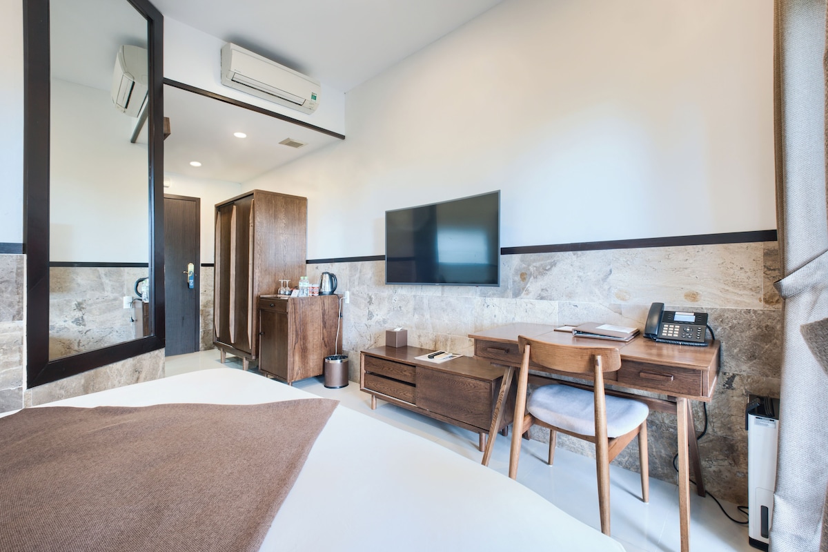 A modern hotel room with a bed, desk, chair, TV, and a bathroom with a shower and toilet.