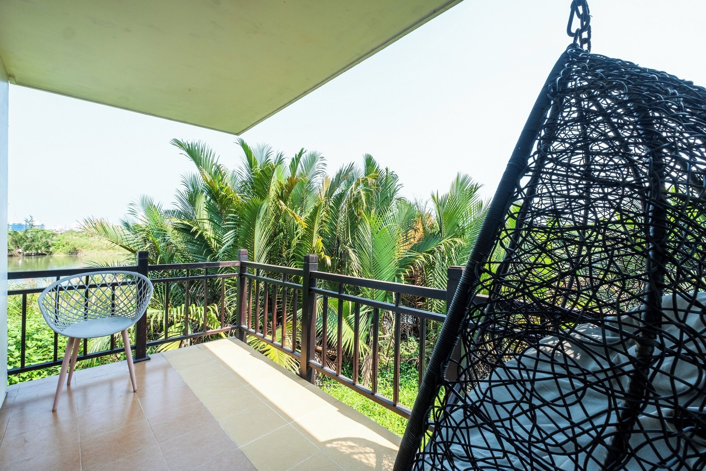 A balcony with a chair, a hanging chair, and a view of palm trees.
