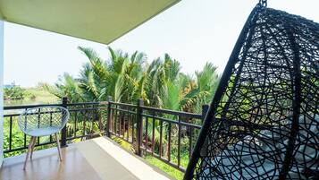 A balcony with a chair, a hanging chair, and a view of palm trees.