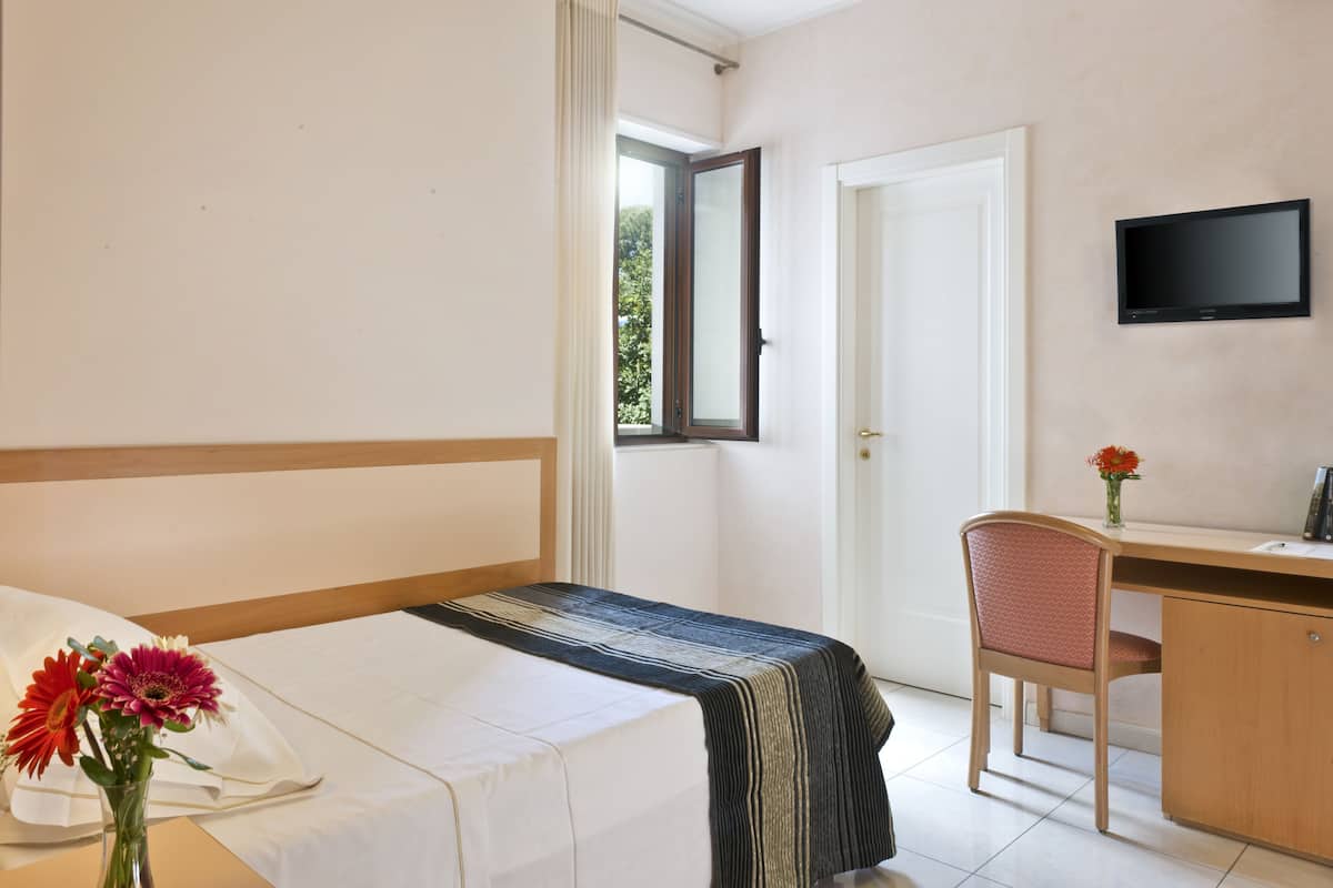 Habitación de hotel con una cama, un escritorio, una silla, un televisor y una ventana.