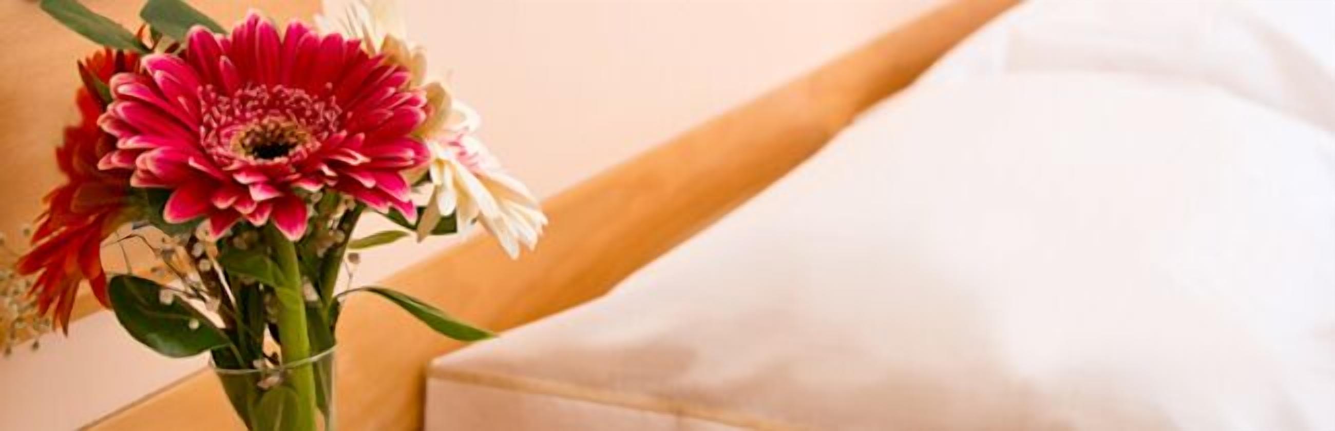 A bed with a white sheet and a vase with flowers.