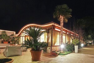A well-lit building with a curved facade, large windows, and a palm tree in the foreground.