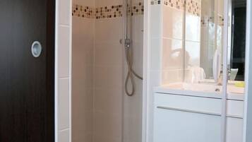 A modern bathroom with a glass-enclosed shower, white tiles, and a vanity with a mirror.