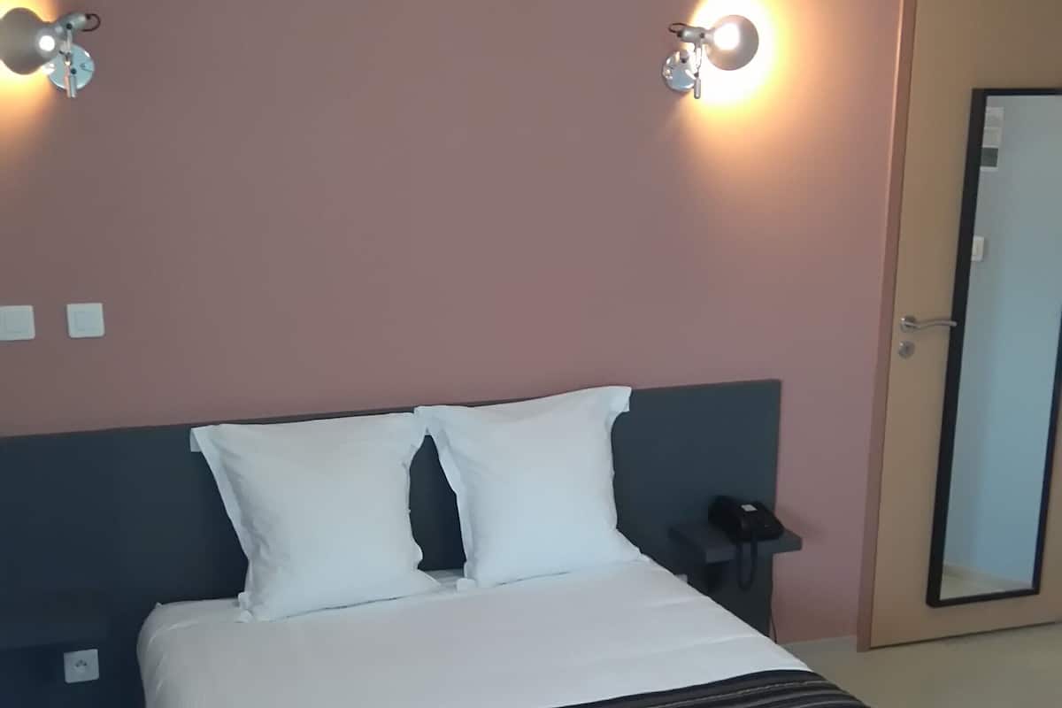 A neatly made bed with white and dark striped bedding, two wall-mounted light fixtures, a bedside table with a phone, and a door with a mirror.