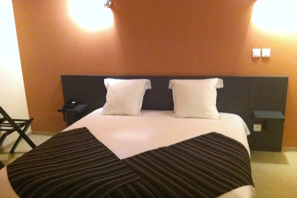 A hotel room with a large bed, two pillows, a nightstand, a chair, and a wall-mounted light fixture.