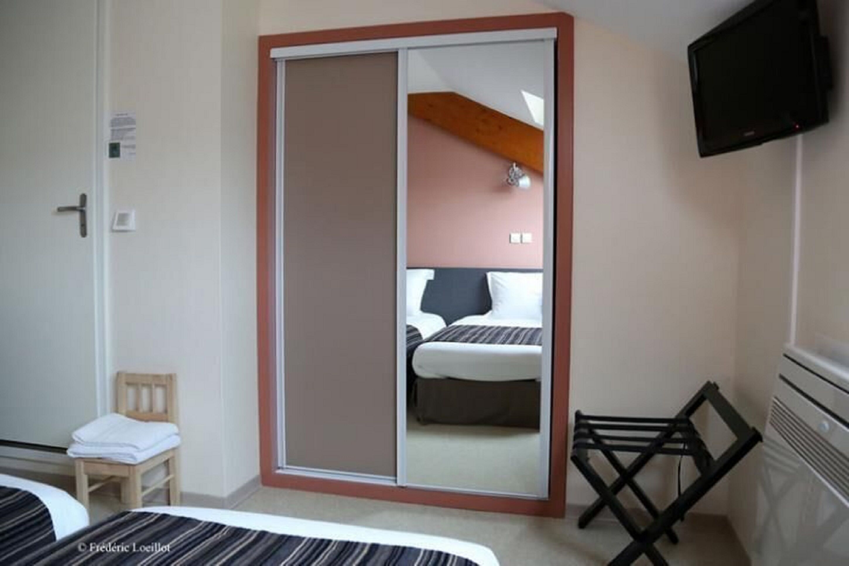 A hotel room with a sliding door closet, a bed, a chair, a TV, and a small table.