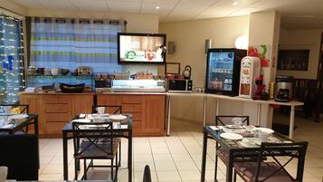 A restaurant with a counter, tables, chairs, a television, a refrigerator, and various kitchen appliances.