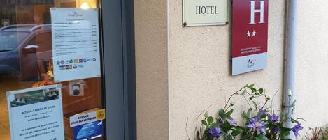 Zona de recepción de hotel con letrero de recepción, señalización con una 'H' que indica habitación accesible para personas con discapacidad y una planta con flores moradas.
