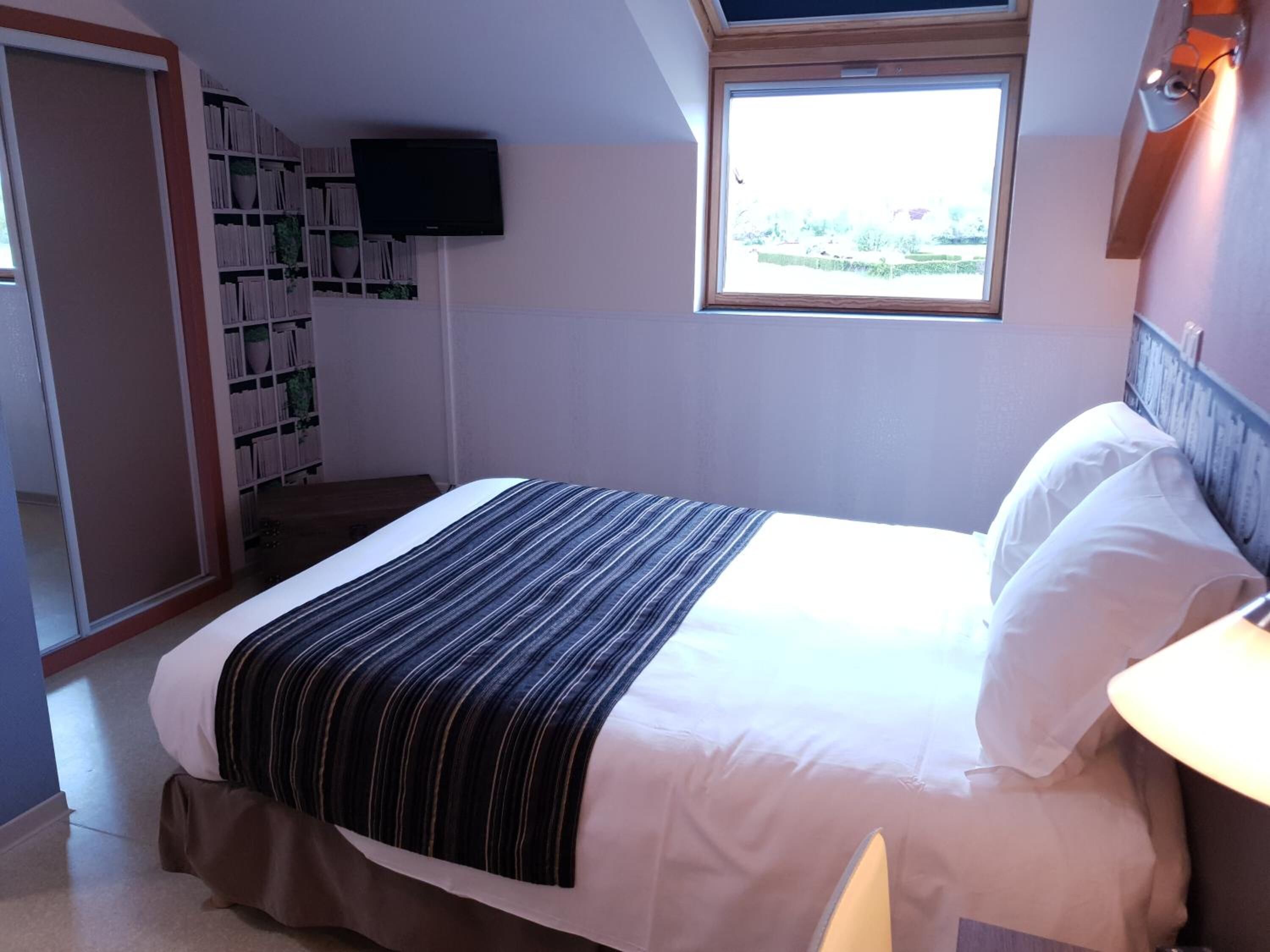 A bedroom with a bed, a window, a bookshelf, and a television.