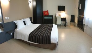 A hotel room with a bed, bedside table, desk, chair, TV, and a small cabinet.