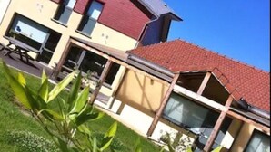 A modern two-story house with a red roof and beige walls, featuring large windows and a visible outdoor seating area. - FASTHOTEL LE RALE DES GENETS - Un hôtel FH COLLECTION  (Dun-sur-Meuse)