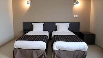A hotel room with two beds, each with a dark headboard and white bedding. There are two wall-mounted light fixtures on either side of the beds.